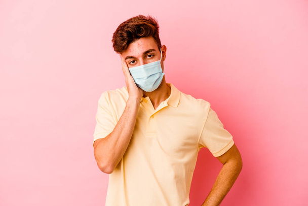 Young caucasian man wearing a protection for coronavirus isolated on pink background who is bored, fatigued and need a relax day. - Photo, Image