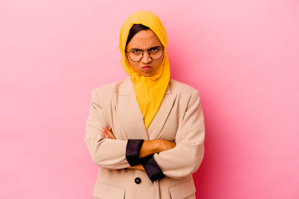 Young business muslim woman isolated on pink background frowning face in displeasure, keeps arms folded. - Photo, Image