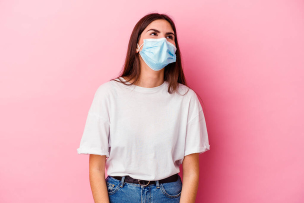 Young caucasian woman wearing a mask for virus isolated on pink background relaxed and happy laughing, neck stretched showing teeth. - Photo, Image