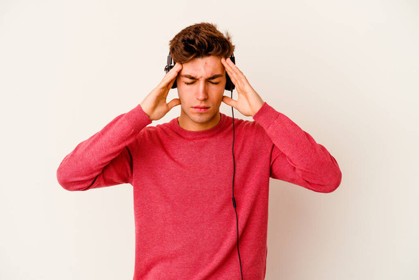 Young caucasian man listening to music isolated on white background touching temples and having headache. - Фото, зображення