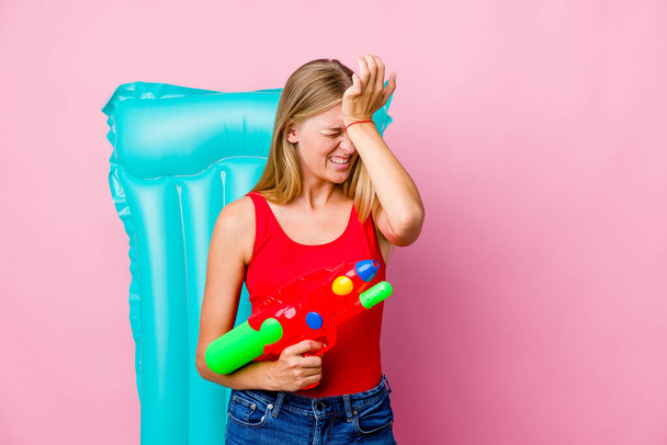 Young russian woman playing with a water gun with an air mattress forgetting something, slapping forehead with palm and closing eyes. - Photo, Image