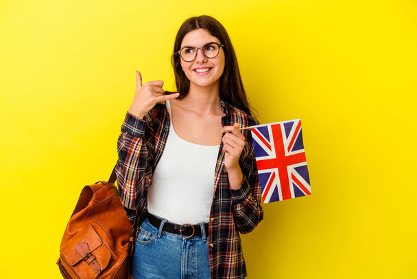 Jeune femme étudiant l'anglais isolé sur fond rose montrant un geste d'appel téléphonique mobile avec les doigts. - Photo, image