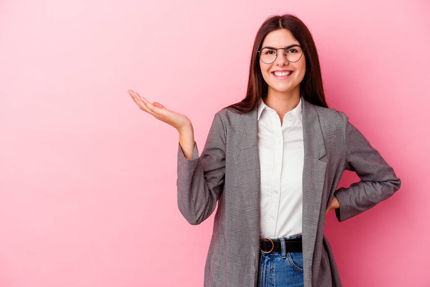 Young caucasian business woman isolated on pink background showing a copy space on a palm and holding another hand on waist. - Fotoğraf, Görsel