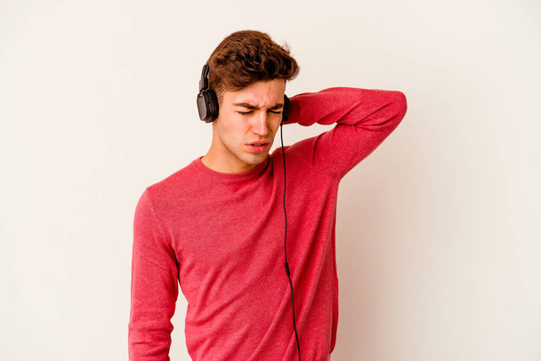 Hombre caucásico joven escuchando música aislada sobre fondo blanco sufriendo dolor de cuello debido a estilo de vida sedentario. - Foto, Imagen