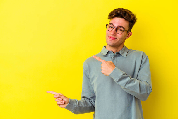 Jonge blanke man geïsoleerd op gele achtergrond wijzend met wijsvingers naar een kopieerruimte, uitdrukken van opwinding en verlangen. - Foto, afbeelding