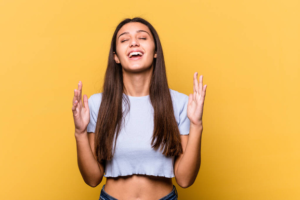 Young Indian woman isolated on yellow background laughs out loudly keeping hand on chest. - Фото, изображение