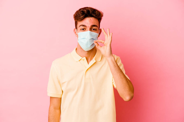Jonge blanke man draagt een bescherming voor coronavirus geïsoleerd op roze achtergrond met vingers op de lippen die een geheim houden. - Foto, afbeelding