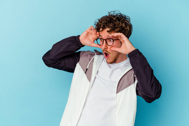 Jeune homme caucasien portant des lunettes isolées sur fond bleu gardant les yeux ouverts pour trouver une opportunité de succès. - Photo, image