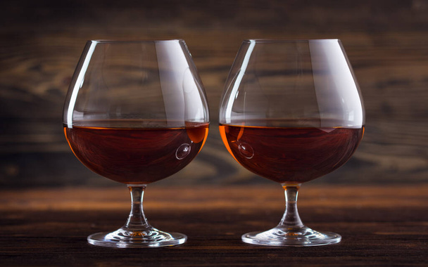 Twee glazen cognac, cognac of whisky op een natuurlijke houten ondergrond. Klassiek cognac glas. Alcoholdrank op de balie in het restaurant.  - Foto, afbeelding