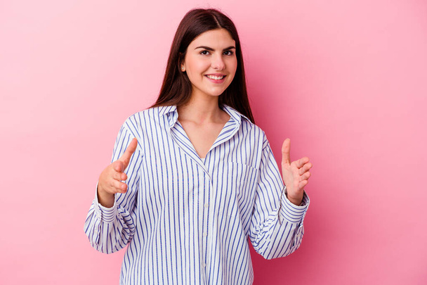 Young caucasian woman isolated on pink background holding something with both hands, product presentation. - Photo, Image