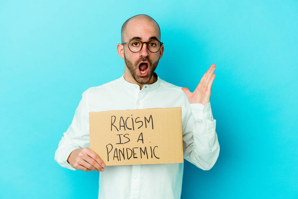 Young caucasian bald man holding a racism is a pandemic isolated on white background surprised and shocked. - Photo, Image