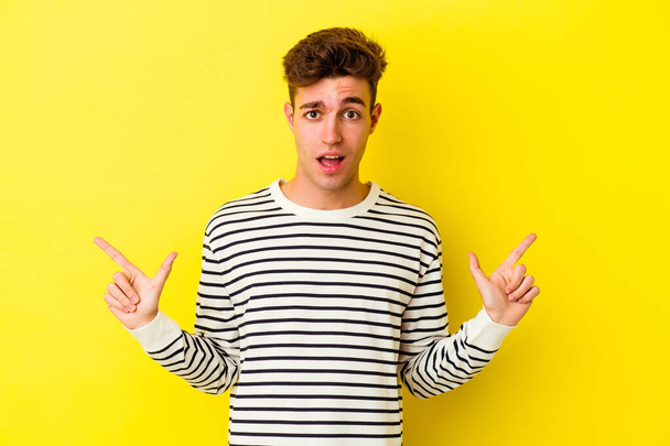 Νεαρός καυκάσιος άνδρας απομονωμένος σε κίτρινο φόντο δείχνοντας διαφορετικούς χώρους αντιγράφων, επιλέγοντας έναν από αυτούς, δείχνοντας με το δάχτυλο. - Φωτογραφία, εικόνα