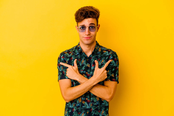 Fiatal fehér férfi visel hawaii ing elszigetelt sárga háttér pontok oldalirányban, próbál választani két lehetőség. - Fotó, kép