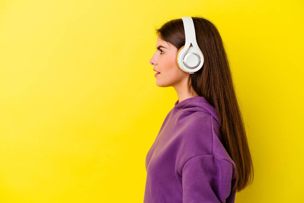 Młoda kaukaska kobieta słucha muzyki ze słuchawkami odizolowanymi na różowym tle patrząc w lewo, na boki poza. - Zdjęcie, obraz