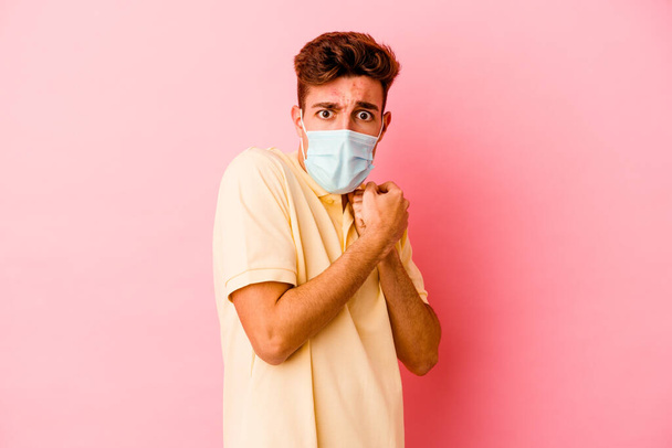 Joven hombre caucásico usando una protección para coronavirus aislado sobre fondo rosa asustado y asustado. - Foto, Imagen
