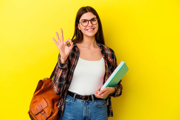 Young student woman isolated on yellow background cheerful and confident showing ok gesture. - Photo, Image