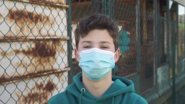 Portret van een gelukkige jongeman met een beschermend medisch masker. Het concept van virusbescherming, naar analogie met een oud ijzeren hek. Stop het coronavirus idee - Video