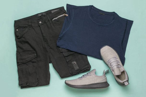 Grijze sneakers, een vrachtbroek en een blauw T-shirt op een blauwe achtergrond. Fashionable jeugd casual kleding. - Foto, afbeelding