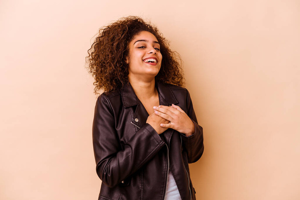 Giovane donna afroamericana isolata su sfondo beige ha un'espressione amichevole, premendo da palmo a petto. Concetto amore. - Foto, immagini