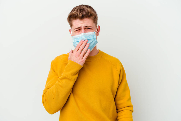 Молодой человек в маске для коронавируса изолирован на белом фоне зевая показывая усталый жест закрывая рот рукой. - Фото, изображение