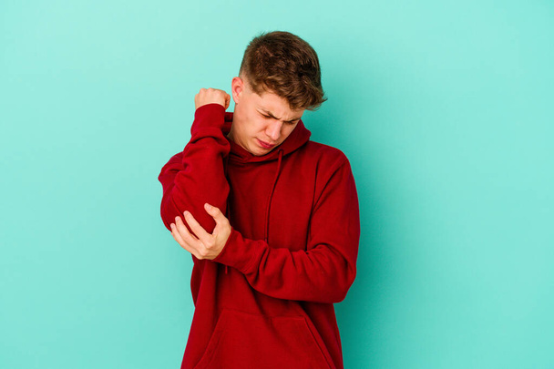 Young caucasian man isolated on blue background massaging elbow, suffering after a bad movement. - Photo, image