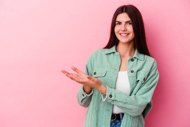 Young caucasian woman isolated on pink background holding a copy space on a palm. - Foto, Bild