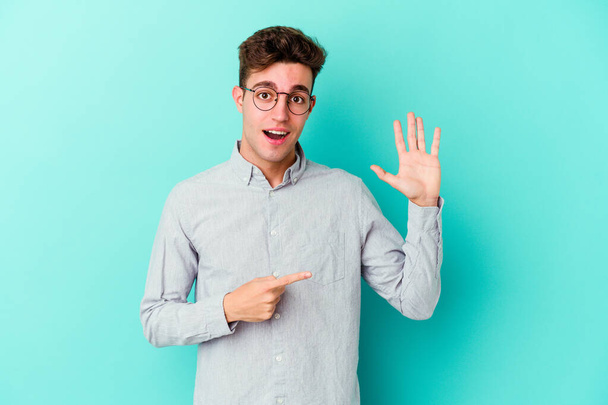 Giovane uomo caucasico isolato su sfondo blu sorridente allegro mostrando numero cinque con le dita. - Foto, immagini