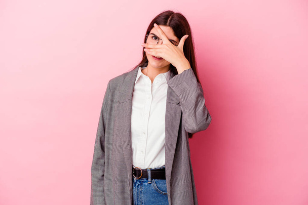 Young caucasian business woman isolated on pink background blink at the camera through fingers, embarrassed covering face. - Photo, Image