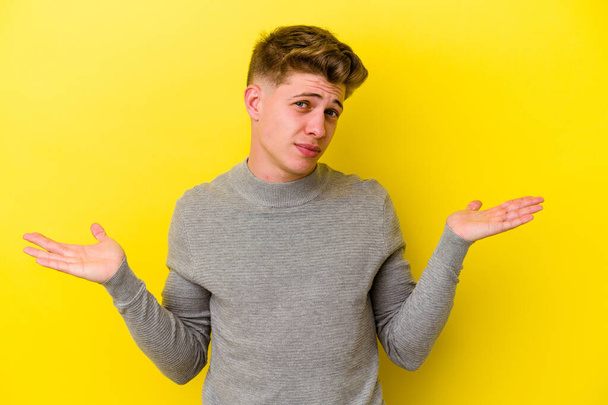 Young caucasian man isolated on yellow background doubting and shrugging shoulders in questioning gesture. - Photo, Image