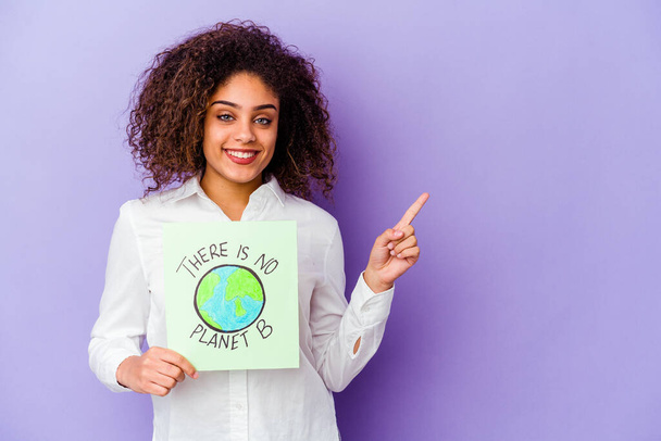 Молода афроамериканська жінка, що тримає плакат із планетою В, не ізольована, усміхається і вказує убік, показуючи щось у порожньому просторі.. - Фото, зображення