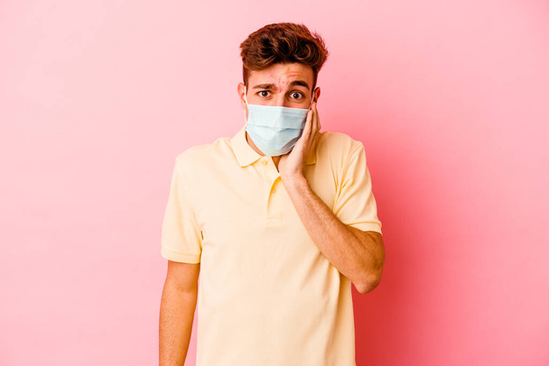 Junger kaukasischer Mann mit Coronavirus-Schutz isoliert auf rosa Hintergrund beißt Fingernägel, nervös und sehr ängstlich. - Foto, Bild