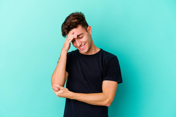 Young caucasian man isolated on blue background blink at the camera through fingers, embarrassed covering face. - Photo, Image