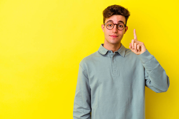 Fiatal fehér férfi izolált sárga háttér mutatja első számú ujját. - Fotó, kép