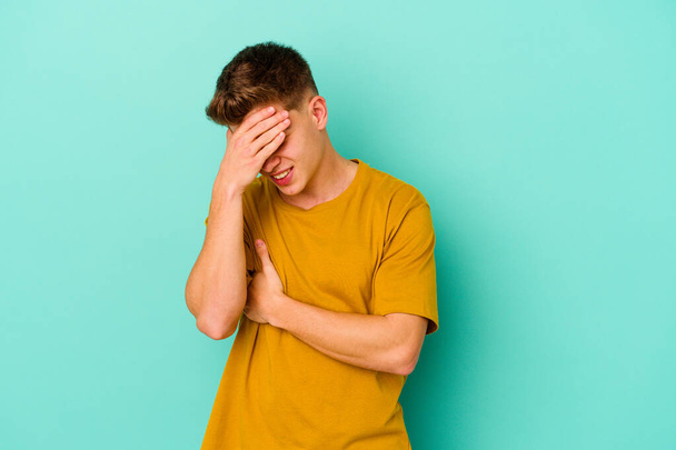 Young caucasian man isolated on blue background blink at the camera through fingers, embarrassed covering face. - Photo, Image