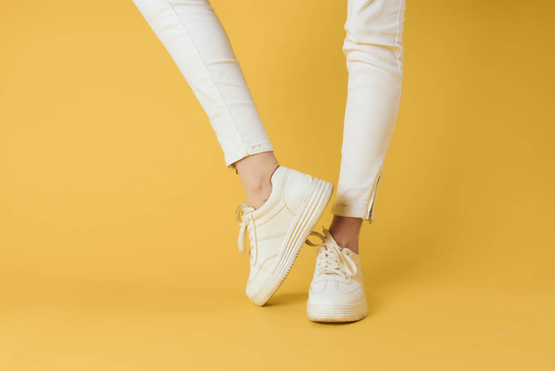 Dámské nohy bílé kalhoty tenisky módní oblečení luxusní ulice styl žluté pozadí - Fotografie, Obrázek