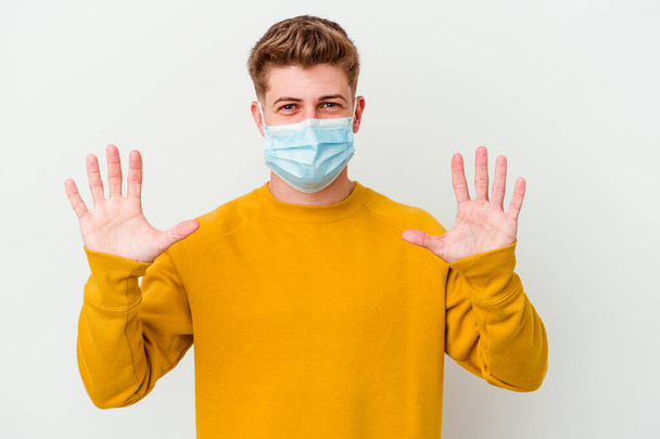 Jeune homme portant un masque pour coronavirus isolé sur fond blanc montrant le numéro dix avec les mains. - Photo, image