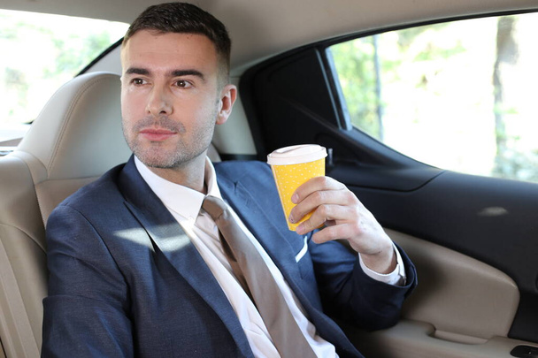車の後部座席にコーヒーの紙コップとハンサムな若いビジネスマンのクローズアップ肖像画 - 写真・画像