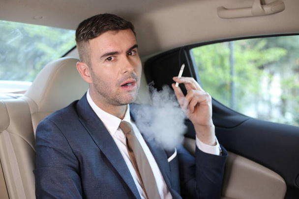 primer plano retrato de joven hombre de negocios guapo fumando cigarrillo en el asiento trasero del coche - Foto, imagen