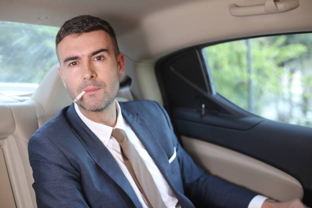 車の後部座席でハンサムな若いビジネスマンの喫煙タバコのクローズアップ肖像画 - 写真・画像