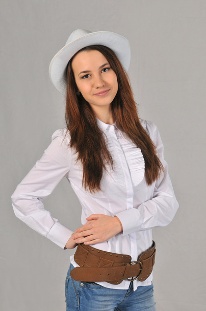 A girl in a white hat, white shirt, jeans and cowboy belt holding his right hand on the belt - Foto, Bild
