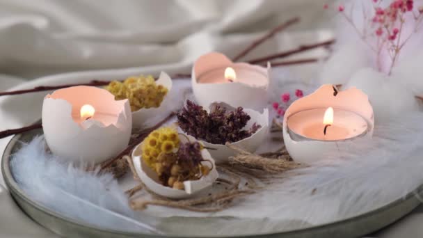 Trendy Easter decorations. Cracked organic eggs with dry grass flowers on plate. Candle light in White shell of the eggs. Bird feather. Burning candles flame smoke - Footage, Video