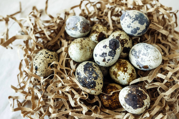 Маленькие пятнистые перепелиные яйца в бумажном гнезде. Простой декор к Пасхе. вид сверху, селективная фокусировка - Фото, изображение