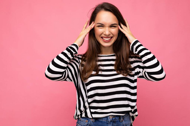 Foto van jong positief gelukkig glimlachen mooi brunette vrouw met oprechte emoties dragen casual gestreepte trui geïsoleerd op roze achtergrond met kopieerruimte - Foto, afbeelding