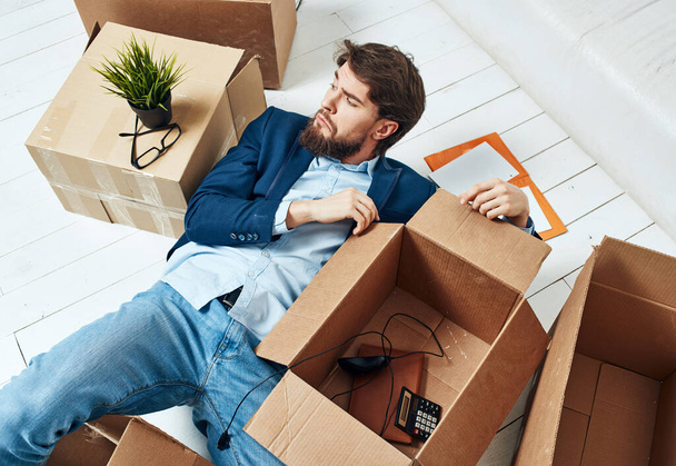 Un uomo con scatole si trova sul pavimento di una stanza di trasloco ufficio disimballaggio - Foto, immagini