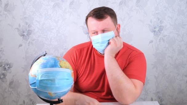 man is sad about the illnesses on the plan and the lack of travel. male looks globe in protective mask and pandemic vaccine. Corona virus treatment concept, injection, clinical trials during a - Footage, Video