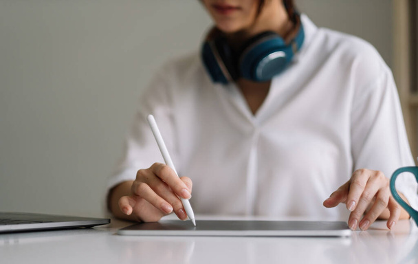 Közelkép a női munkavállaló dolgozik otthonról digitális tabletta, laptop és fülhallgató az otthoni irodai szobában - Fotó, kép