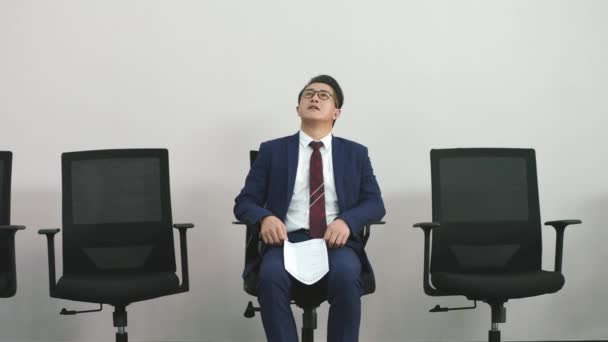 γηραιότερος Ασιάτης επιχειρηματίας κάθεται στην καρέκλα περιμένοντας τη σειρά του να του πάρουν συνέντευξη δείχνοντας απογοητευμένος και αβέβαιος - Πλάνα, βίντεο