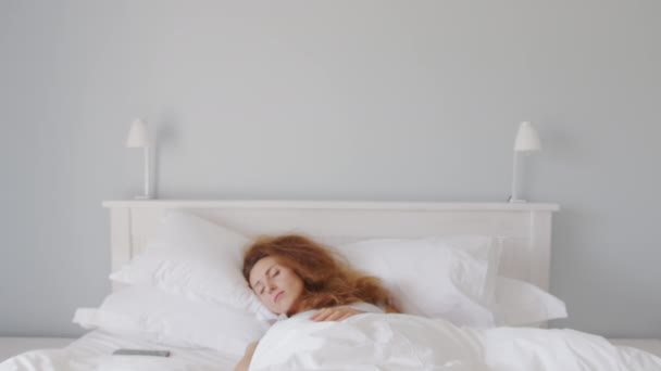Close-up shot van slaperige blanke vrouw wakker in de ochtend, het nemen van smartphone en het uitschakelen van de wekker om meer slaap te krijgen. - Video