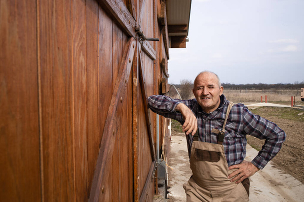 Portret van een boer die bij houten boerderijdeuren staat op een boerderij voor huisdieren. - Foto, afbeelding