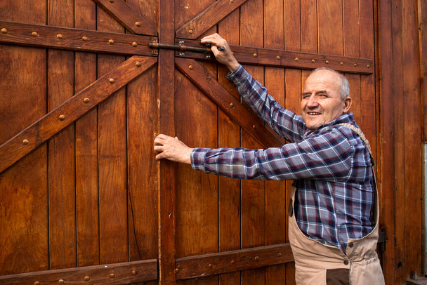 Portrait of farmer opening wooden farmhouse doors at domestic animals farm. - Photo, Image